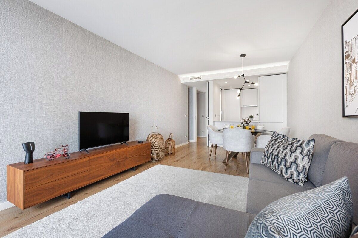 En moderne stue med et fladskærms-tv, en træunderholdningsenhed, en grå sofa og et spiseområde med et hvidt bord og stole.