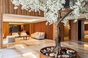 Un intérieur moderne avec un grand arbre, des murs recouverts de panneaux en bois et un espace salon agrémenté de canapés et de poufs.