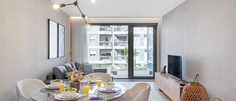 A modern dining area with a glass table, white chairs, and a view of a balcony with buildings.