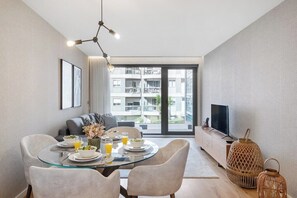 Ein moderner Essbereich mit einem Glastisch, weißen Stühlen und Blick auf einen Balkon mit Gebäuden.