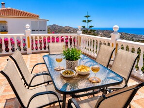 A table with chairs, a bowl of olives, a glass of wine, and a potted plant on a balcony with a view of the sea and mountains. - Villa Cecilia con Vistas by At Home Costa del Sol (Torrox)