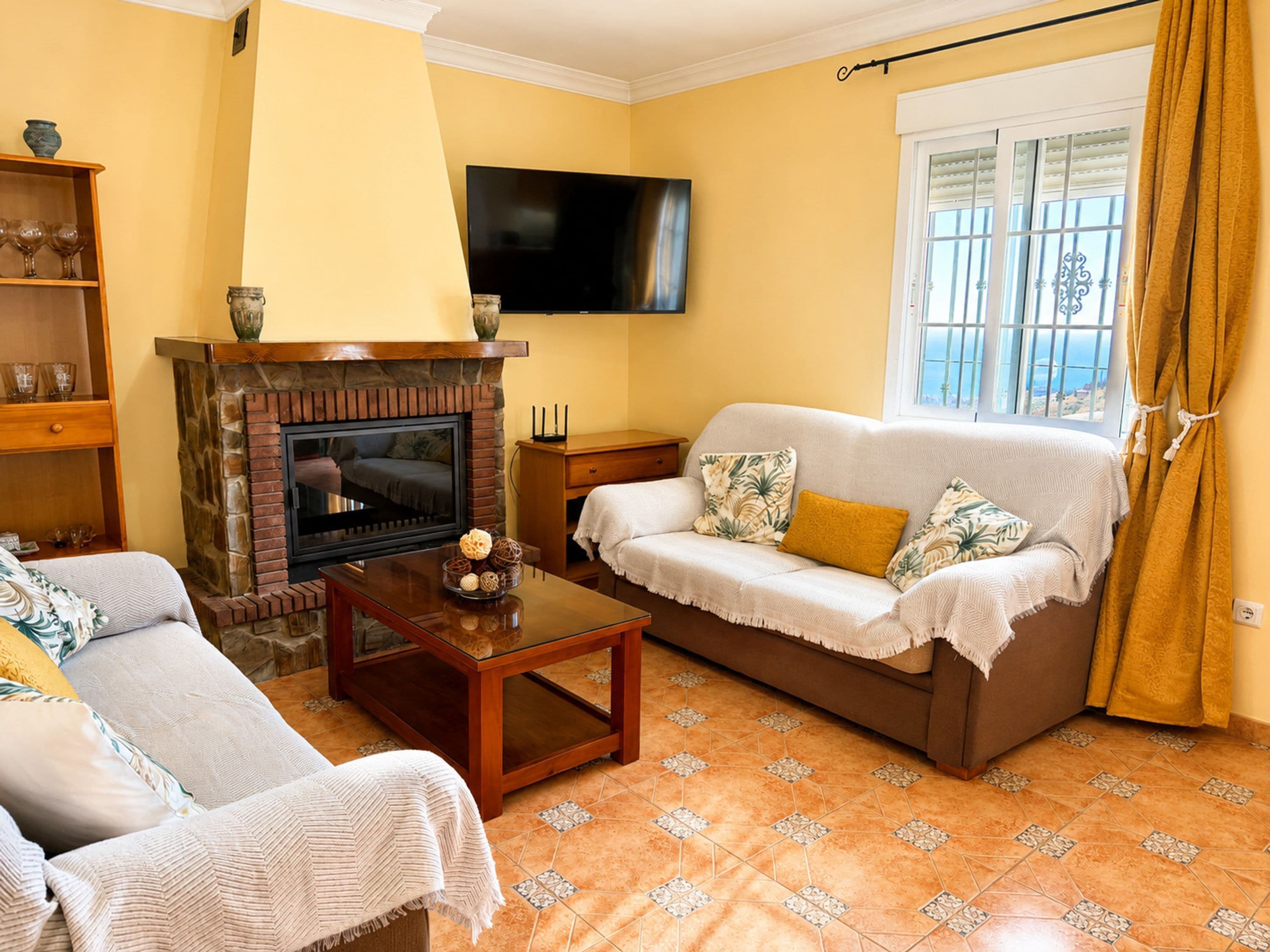 A living room with a fireplace, a sofa, a television, and a window with curtains.
