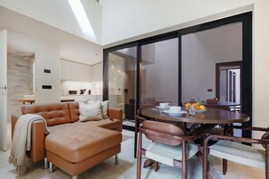A modern living room with a leather sofa, a dining table with chairs, and a large sliding glass door leading to a balcony. - Bonfim Loft with Mezzanine | Terracotta Collection (Porto)