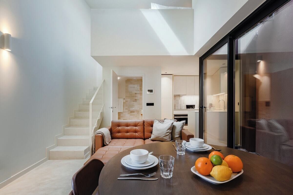 A modern dining area with a table set for two, a staircase leading to an upper level, and a kitchen visible in the background.