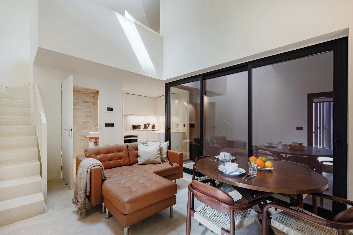 Ein modernes Wohnzimmer mit einem braunen Ledersofa, einem Esstisch mit Stühlen, einer Treppe und einer großen Glasdoor, die in einen anderen Raum führt.