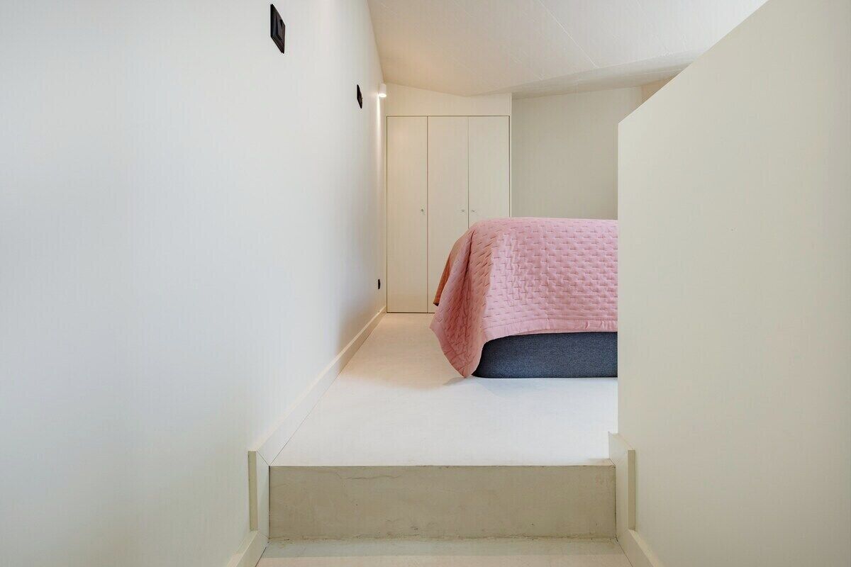 Ein schmaler Flur führt zu einem Schlafzimmer mit Bett, Kleiderschrank und Treppe.
