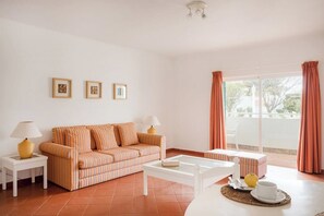 Uma sala de estar com um sofá riscado, uma mesa de centro branca e uma varanda com cortinas.