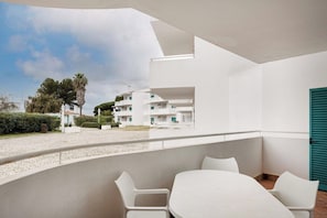 A balcony with white chairs and a table, overlooking a street with buildings and trees. - Prainha 2BR Stay | Pool & Beach Access (Portimão)
