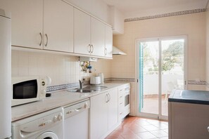 A kitchen with white cabinets, a microwave, a sink, and a dishwasher. - Prainha 2BR Stay | Pool & Beach Access (Portimão)
