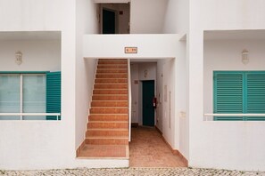 Um edifício com uma escadaria que leva a uma porta marcada 'G 19', um extintor de incêndio e um candeeiro na parede.