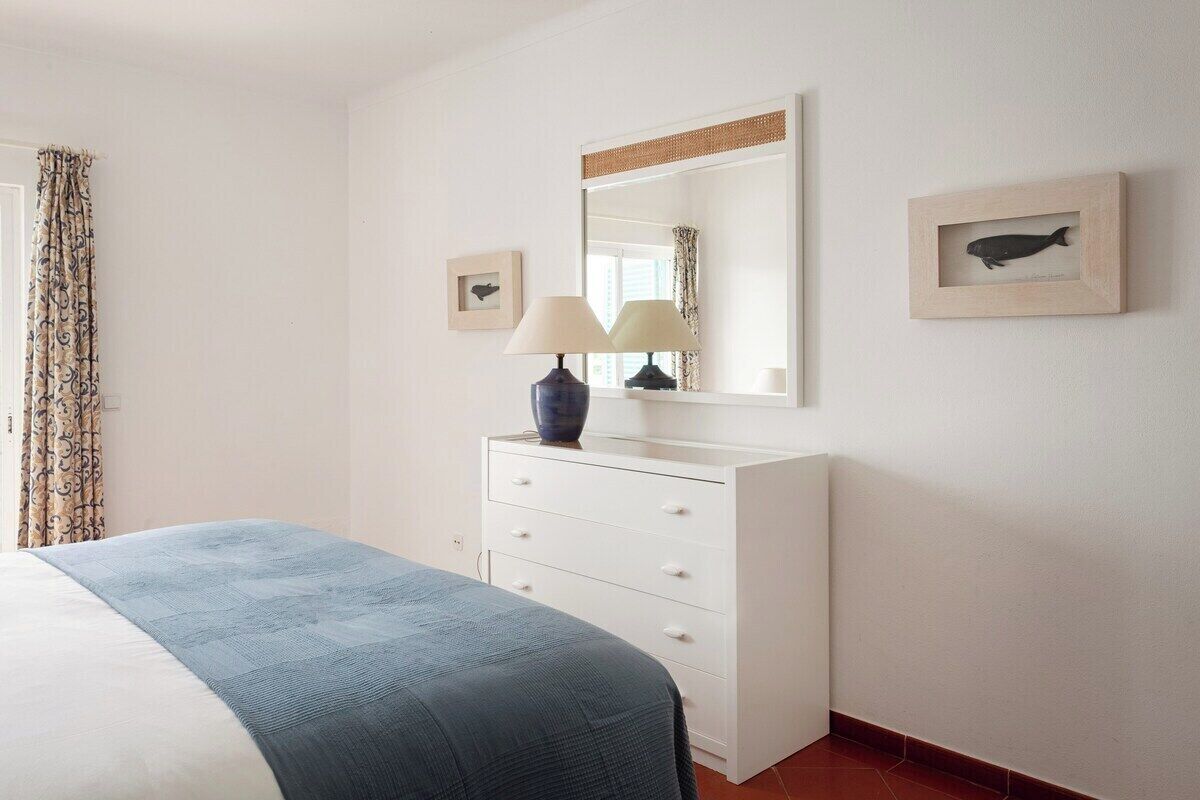 A bedroom with a bed, a dresser, a mirror, and two framed pictures on the wall.
