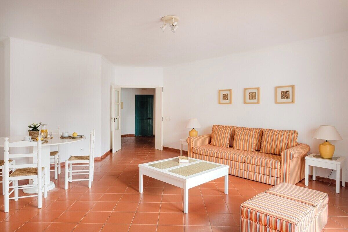 Una sala de estar con una mesa de centro blanca, un sofá a rayas y un comedor con sillas y una mesa blancos.