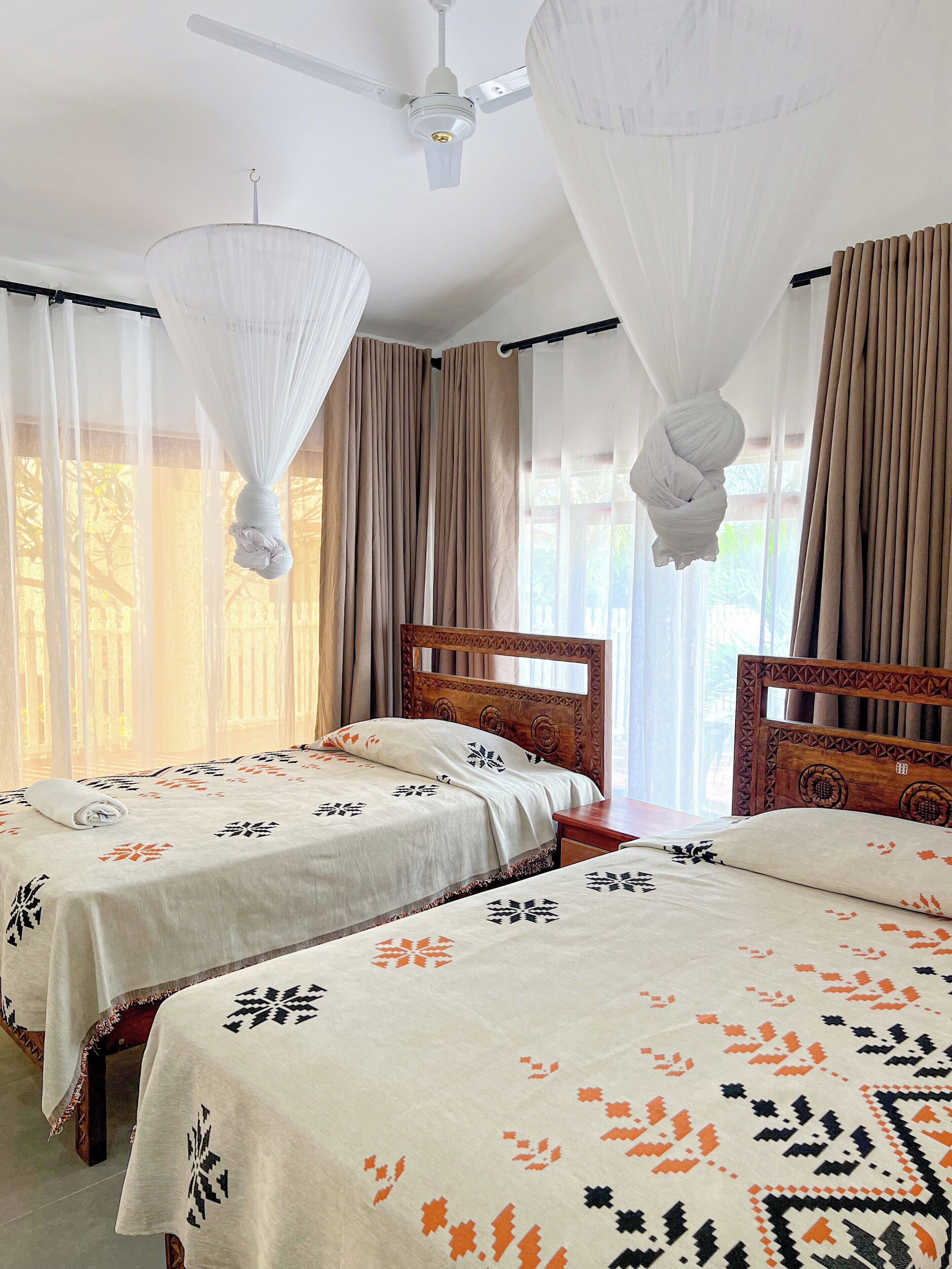 A hotel room with two beds, a ceiling fan, and sheer curtains.