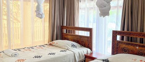 A hotel room with two beds, a ceiling fan, and sheer curtains.