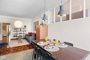 A modern dining area with a wooden table, chairs, and a view of the kitchen. - Porto Unik | Walk to Historical Center (Porto)