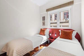 A bedroom with two beds, a window with blinds, a red headboard, and a wall-mounted lamp. - Porto Unik | Walk to Historical Center (Porto)