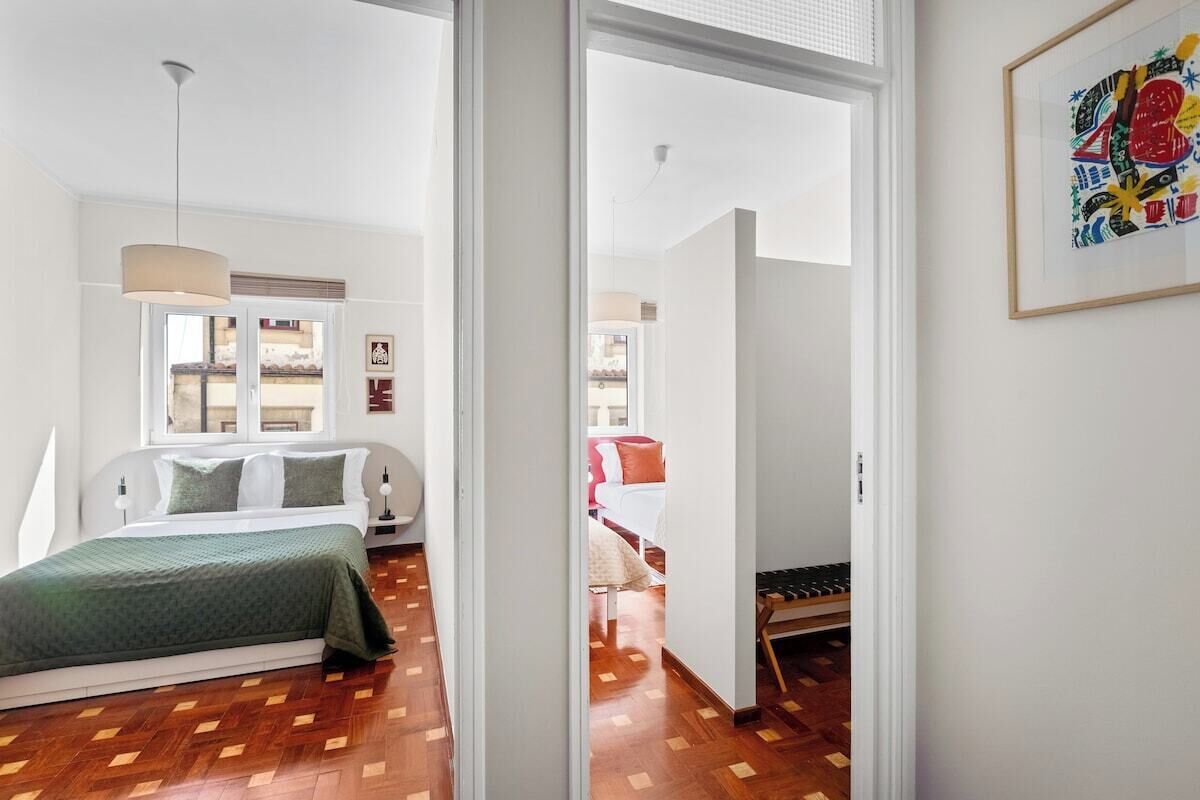 Une chambre à coucher moderne, avec un lit, un luminaire suspendu et une vue sur une autre pièce, accessible par une porte ouverte.