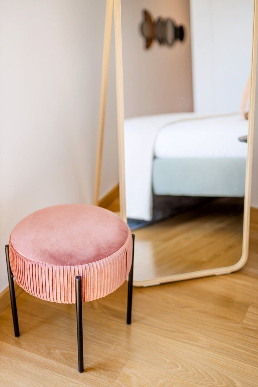 Un tabouret rose, recouvert d’un tissu capitonné et doté d’un motif à rayures, placé devant un miroir à cadre en bois.