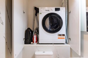 Uma lavanderia compacta com máquina de lavar frontal, secadora compacta e um vaso sanitário pequeno e branco.