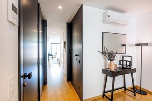 A hallway with a door, a console table with a vase and a lamp, and a large mirror on the wall. - Camões Downtown with Parking (Porto)