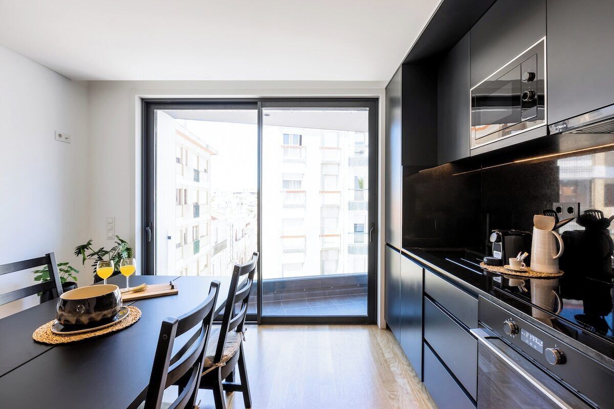 Een moderne keuken met een groot raam, een eettafel met stoelen en een koffieapparaat.