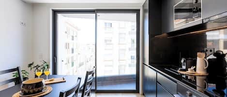A modern kitchen with a large window, a dining table with chairs, and a coffee machine.