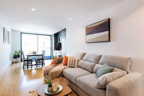 A modern living room with a sofa, a coffee table, and a dining area with chairs and a table. - Camões Downtown with Parking (Porto)