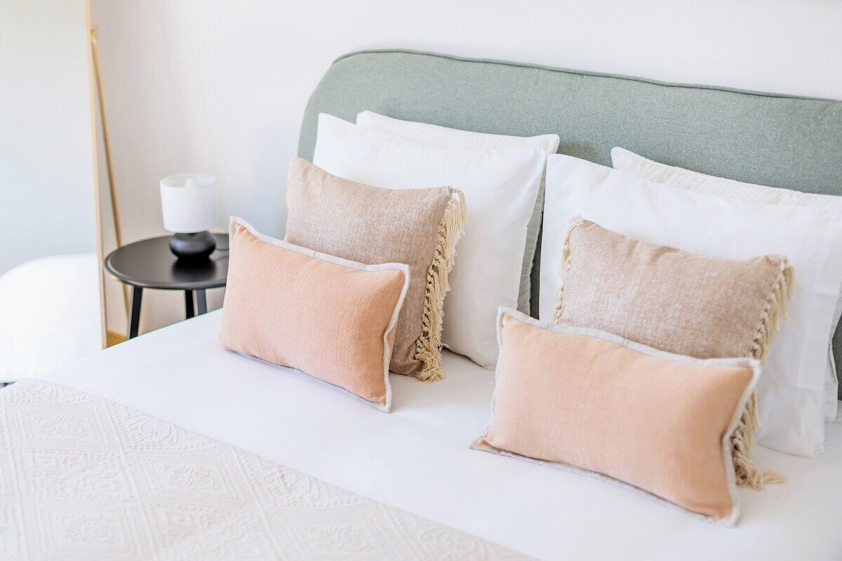 Una cama bien tendida con cabecera verde, ropa de cama blanca y almohadas color beige.