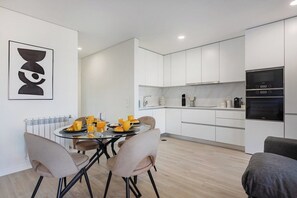 A modern kitchen with white cabinets, a dining table with chairs, and a black oven. - The Pine Flat with Pool @ Furadouro (Ovar)