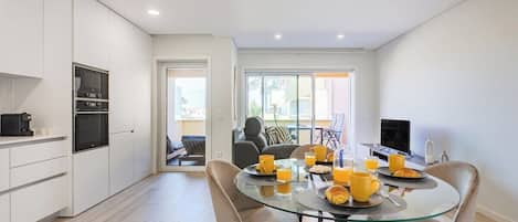A modern kitchen with white cabinets, a glass dining table, and a seating area with a sofa and chairs.