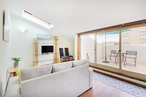 Una sala de estar moderna con sofá, televisor, zona de estar, puertas correderas de vidrio que dan a un balcón y una pequeña mesa con una planta.