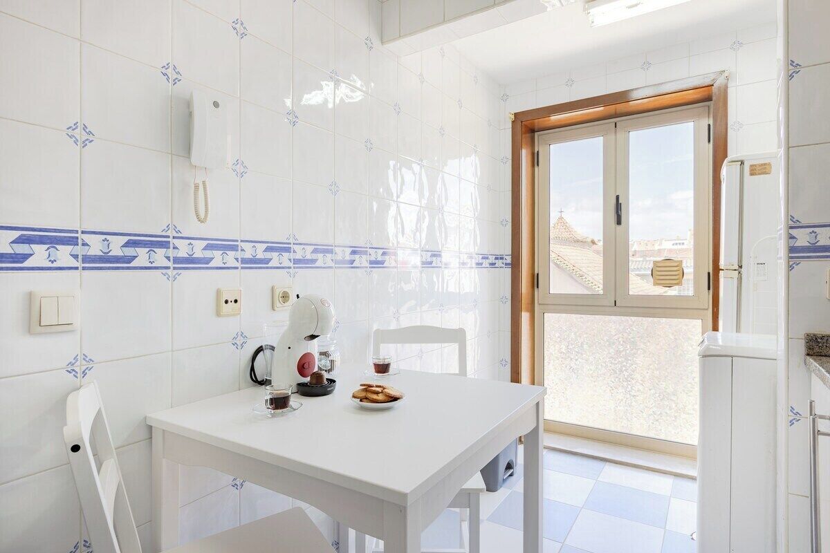 A small kitchen with a white table, a coffee machine, a kettle, and a plate of cookies.