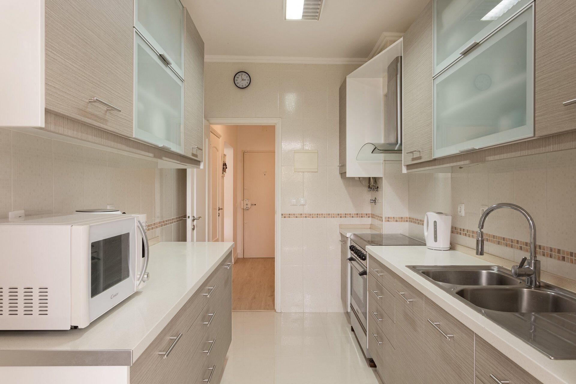 A modern kitchen with white cabinetry, a microwave, a kettle, and a stainless steel sink.