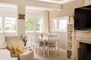 A living room with a fireplace, a television, a dining table with chairs, a sofa, and a window with curtains. - The Cascais Hideaway (Cascais)
