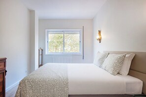 Ein Schlafzimmer mit einem Bett, einem Fenster, einer Wandleuchte und einer Holzkommode.