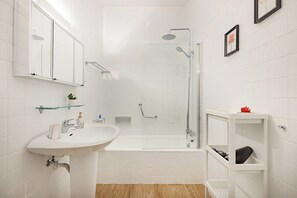 Ein modernes Badezimmer mit einer in Glas eingefassten Dusche, einem weißen Waschbecken und einem Waschtisch mit Stauraum.