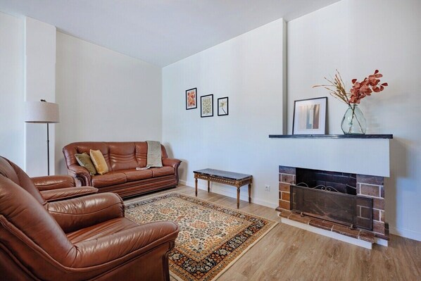Ein Wohnzimmer mit Kamin, Ledersofa, Couchtisch und einem gemusterten Teppich.