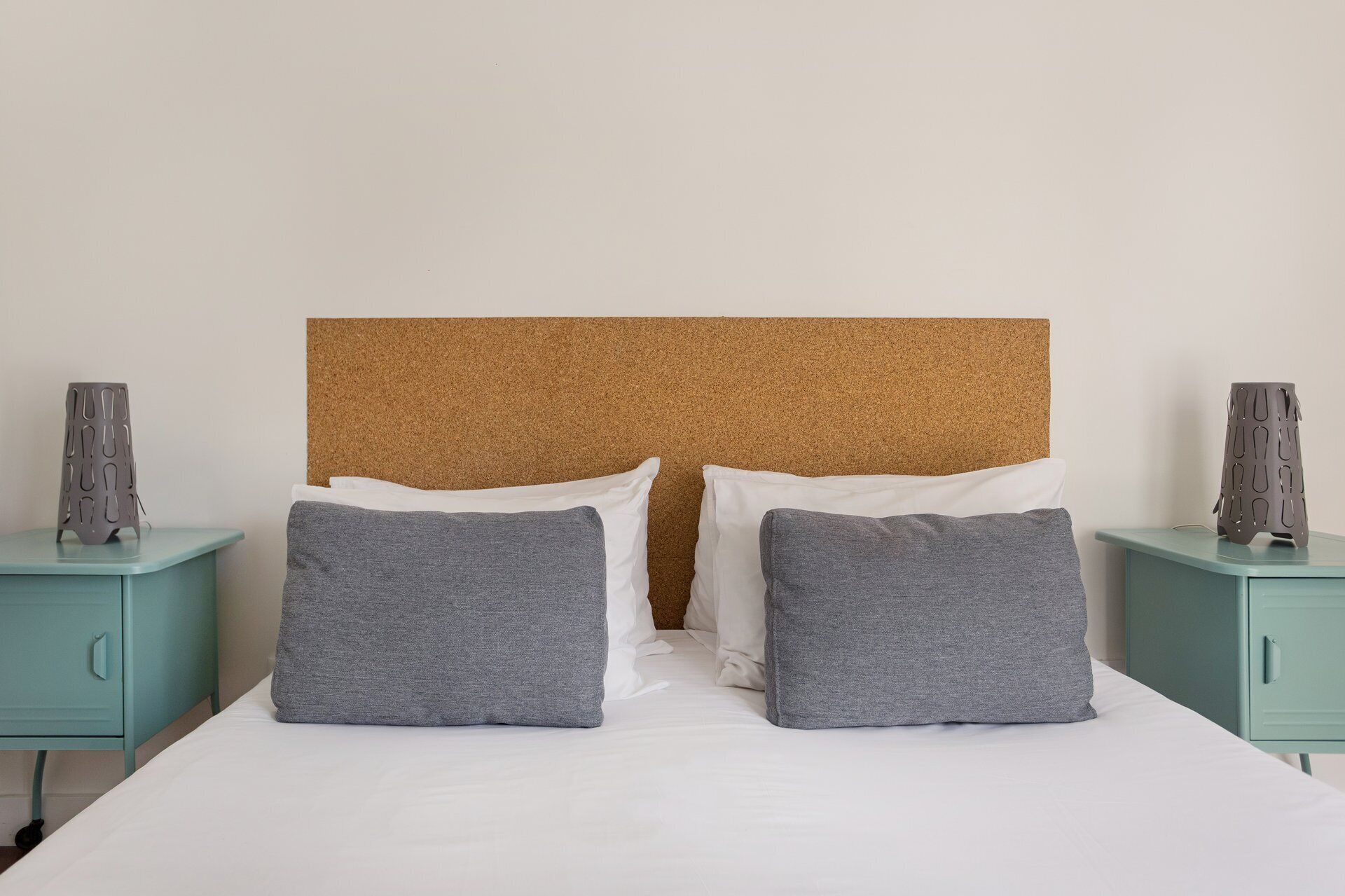 A bed with a cork headboard, two grey pillows, and white sheets.