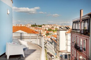 Un balcón con una silla blanca, barandilla y vistas de un paisaje urbano con edificios de techo rojo.
