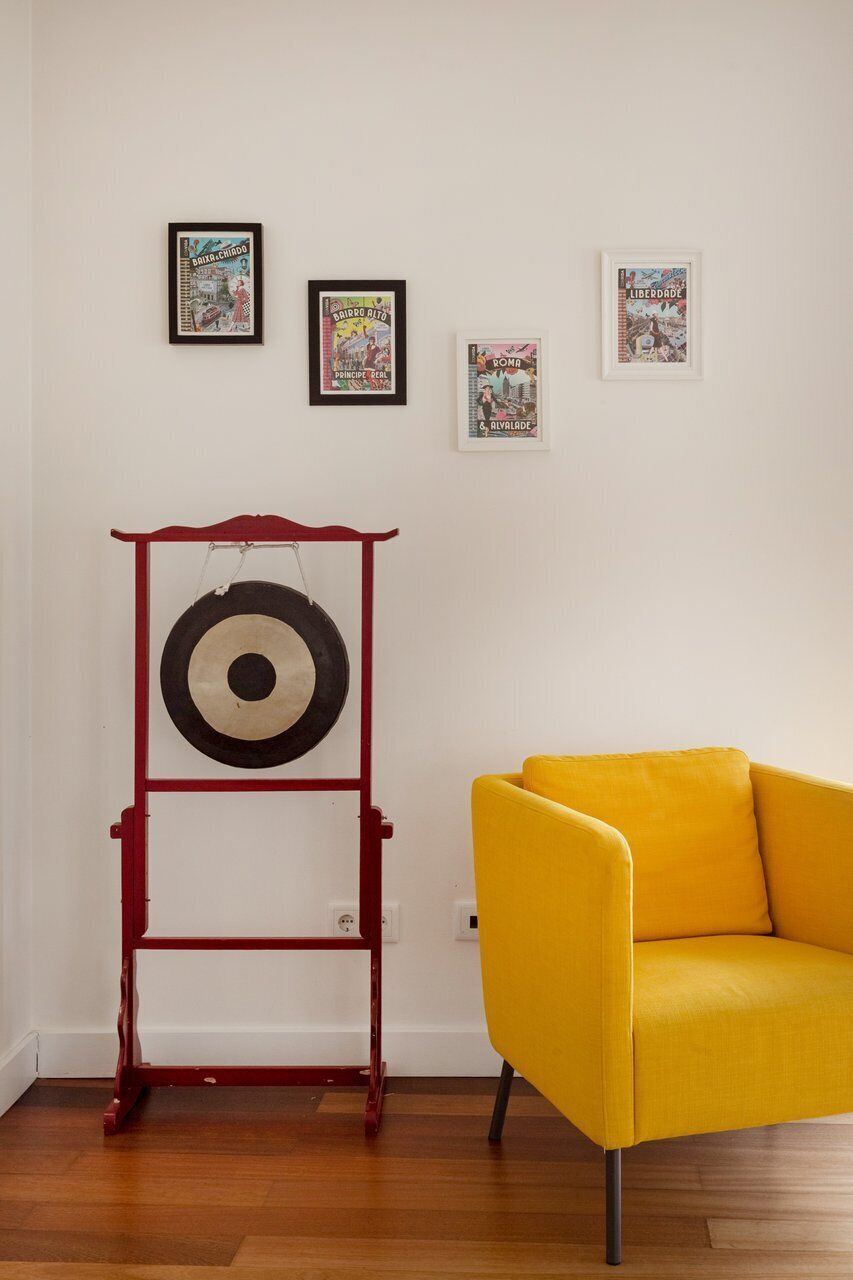 A room with a yellow armchair, a red shelf with a target, and three framed posters on the wall.