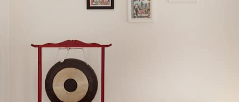 A room with a yellow armchair, a red shelf with a target, and three framed posters on the wall.
