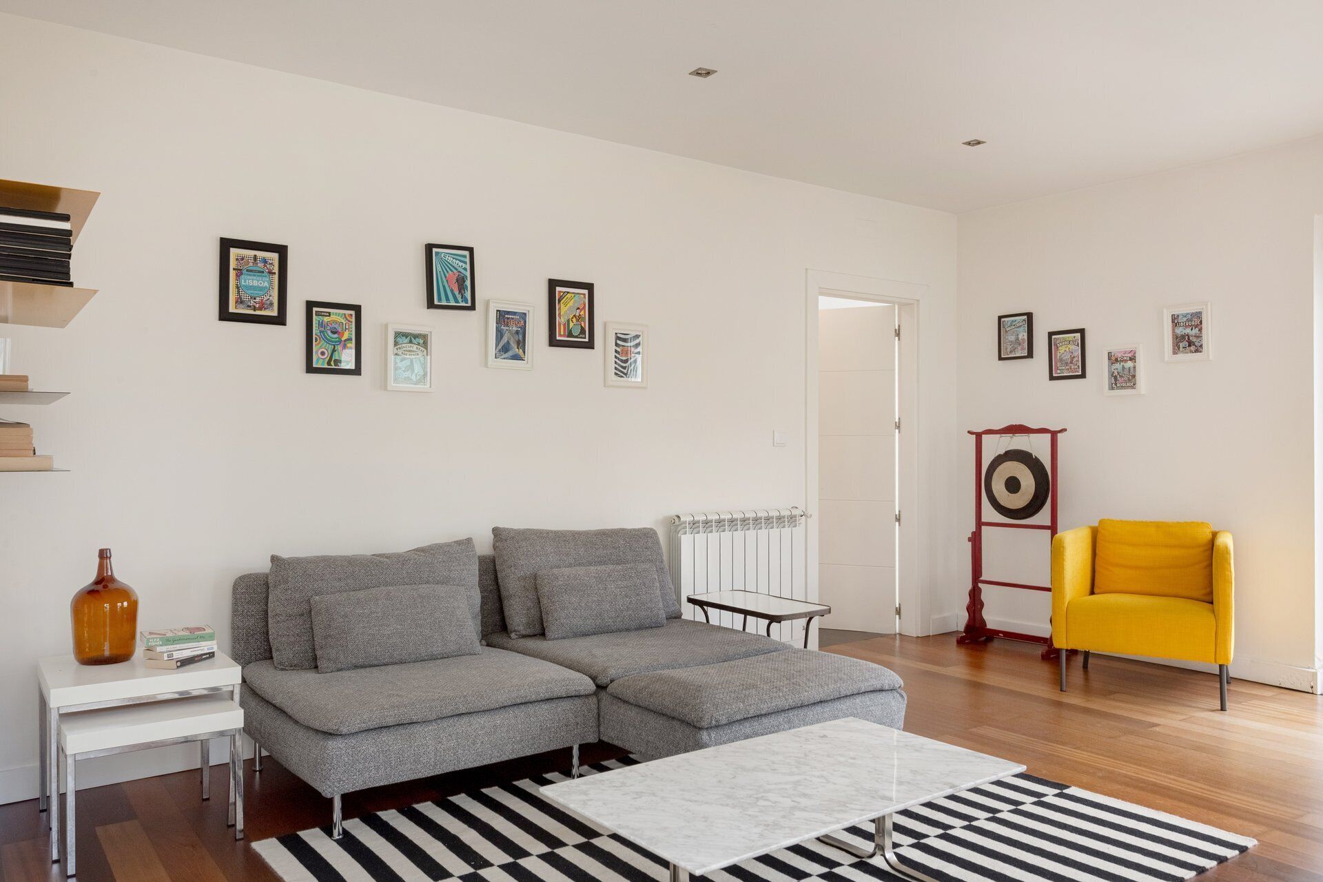 Uma sala de estar moderna com um sofá cinzento, uma poltrona amarela, uma mesa de centro branca e um radiador.