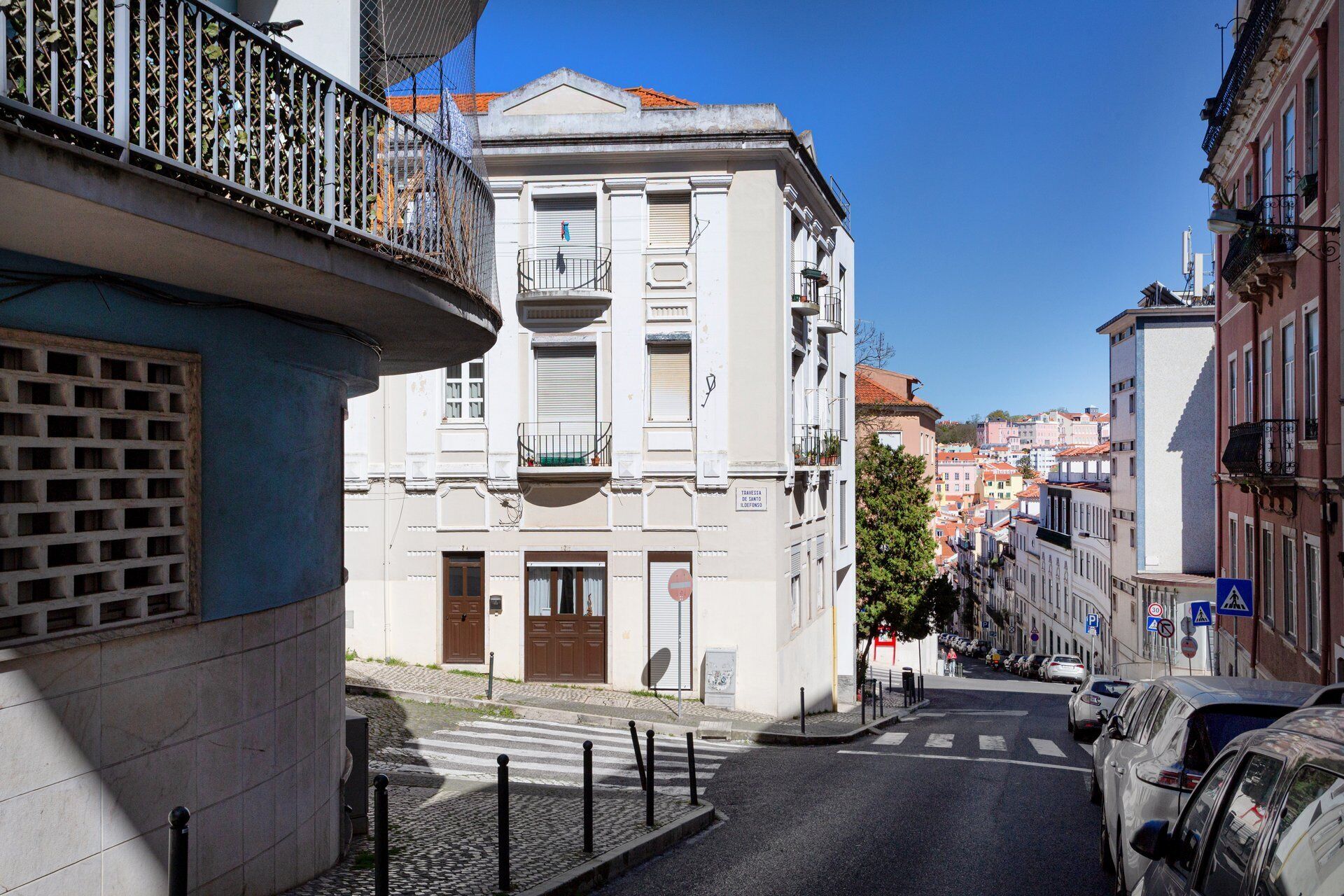 A narrow street with buildings, a pedestrian crossing, and parked cars.