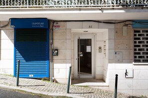 Entrada de edifício com porta de toldo azul identificada com 'SENHOR UVA' e porta com o número '66'.