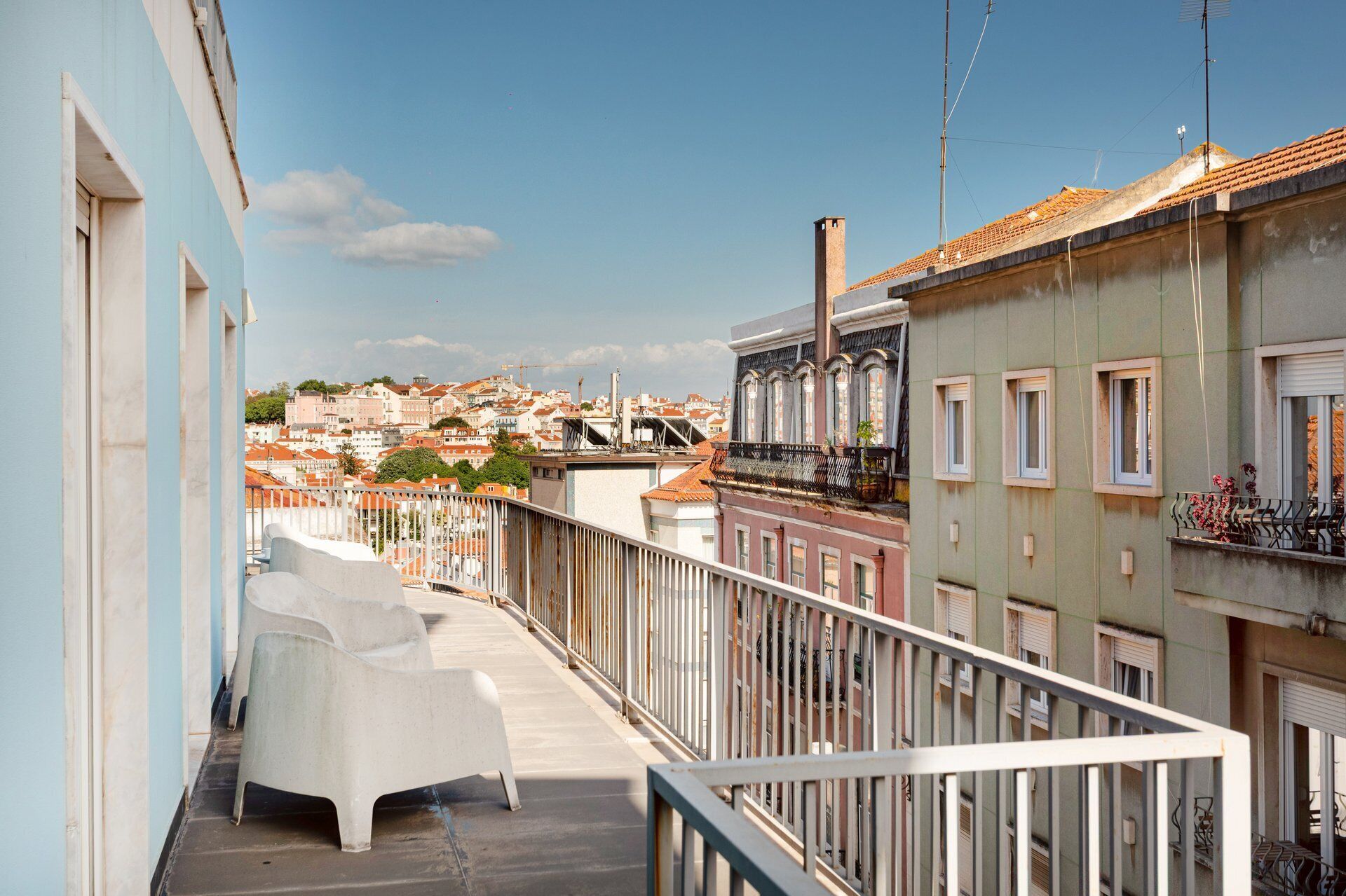 Een balkon met witte stoelen, een hekwerk en een uitzicht op gebouwen in de verte.