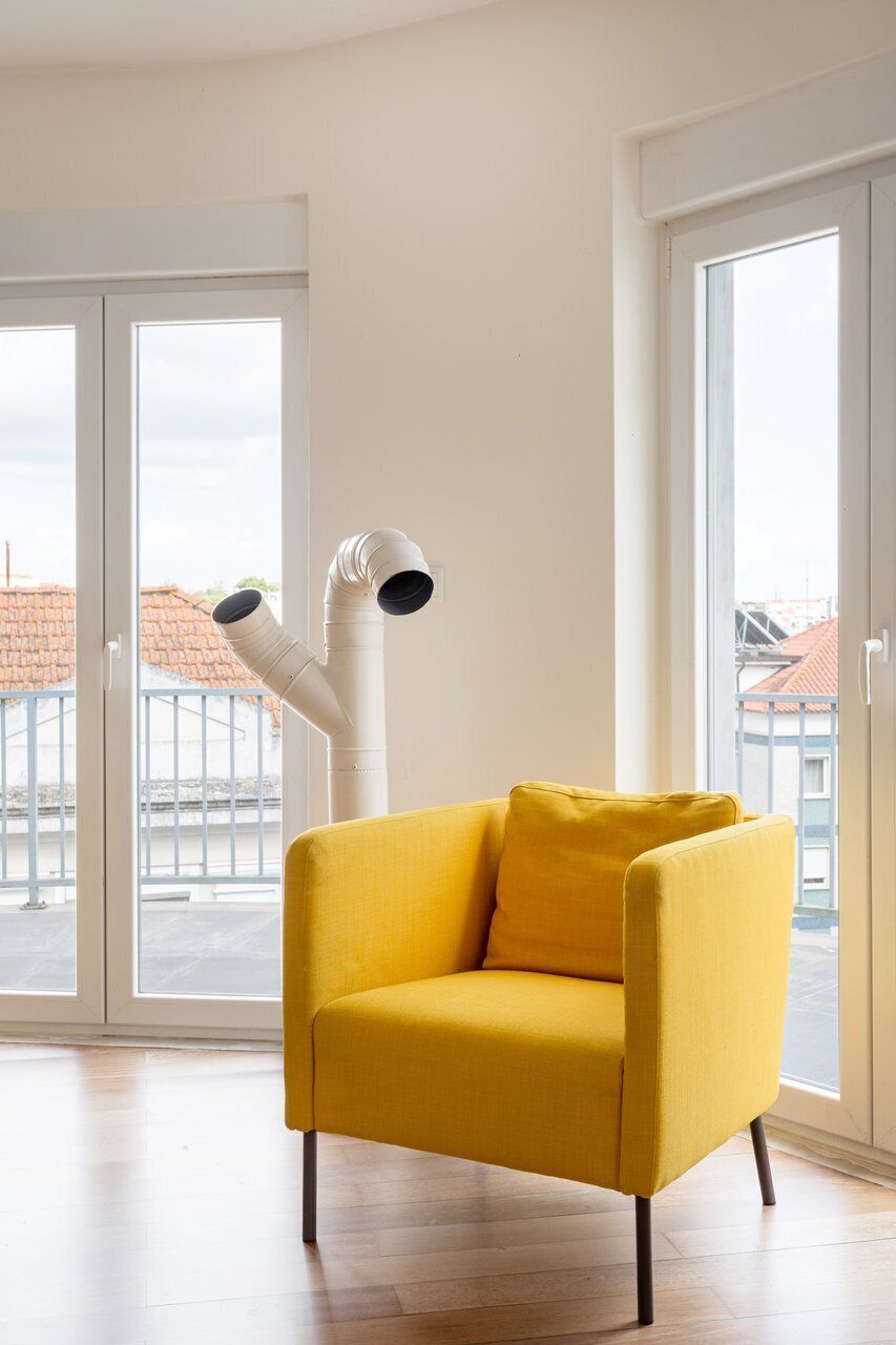 Un sillón amarillo en una habitación con ventanas amplias y una pared blanca.
