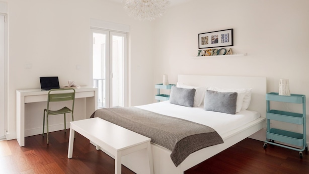 Ein Schlafzimmer mit Bett, Schreibtisch, Stuhl, Bank, Nachttisch und einem an der Wand hängenden Bild.