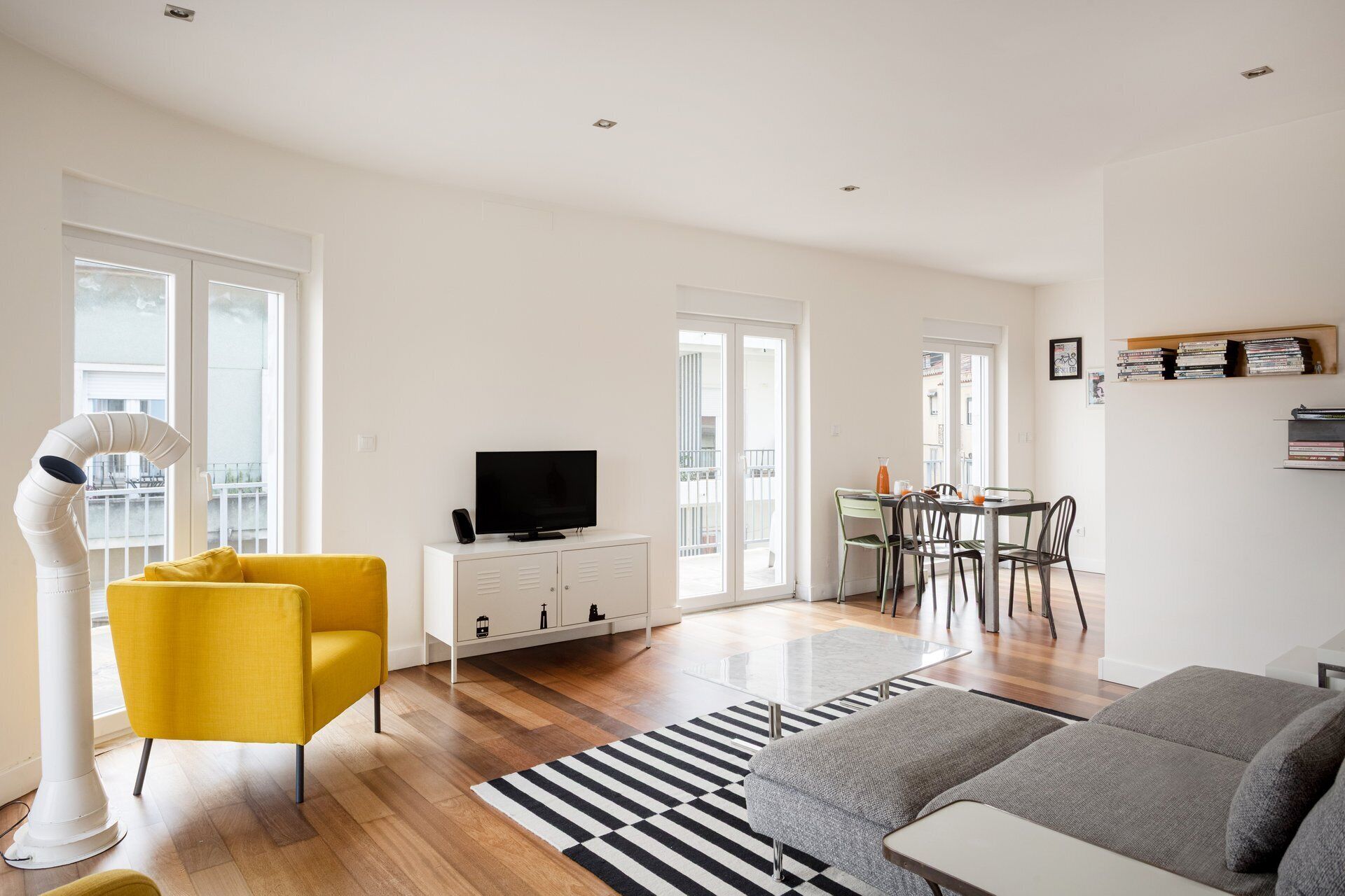 A modern living room with a sofa, a yellow chair, a TV, a dining area with chairs, and a bookshelf.