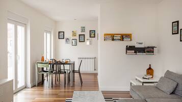 En moderne stue med spiseplads, sofa, bogreoler og en radiator.