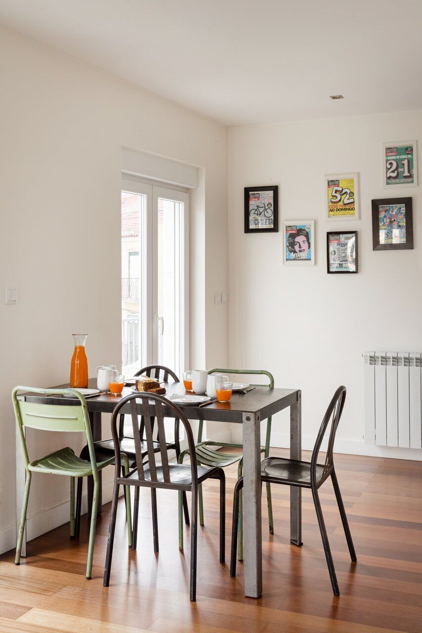 A dining area with a table set for four, chairs, a window, and framed pictures on the wall.